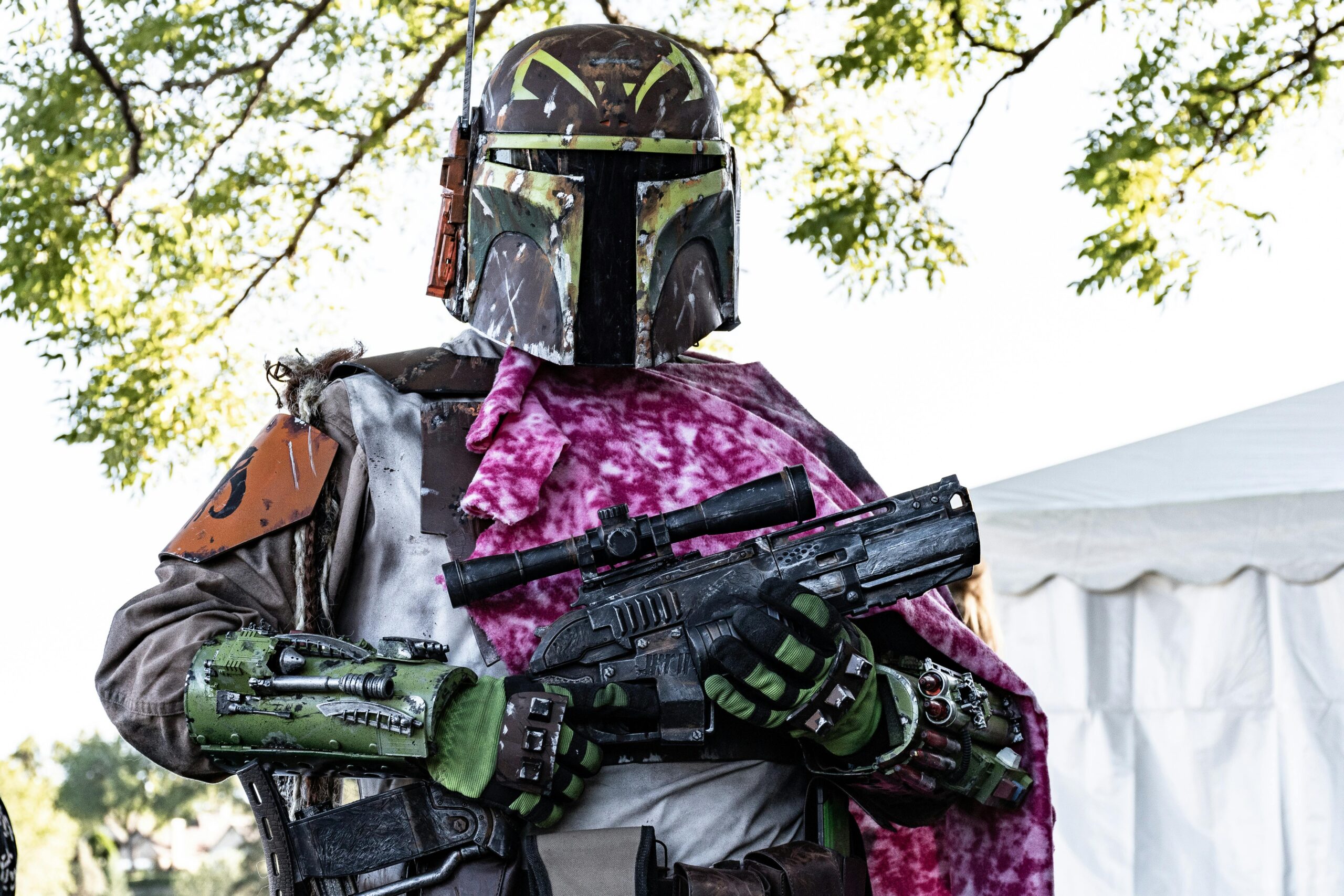 Bounty hunter in detailed Star Wars cosplay with vibrant armor and rifle outdoors.