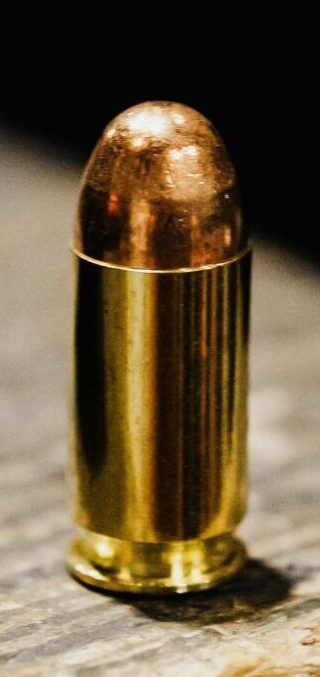 A focused view of a bullet standing upright on a rustic wooden surface.