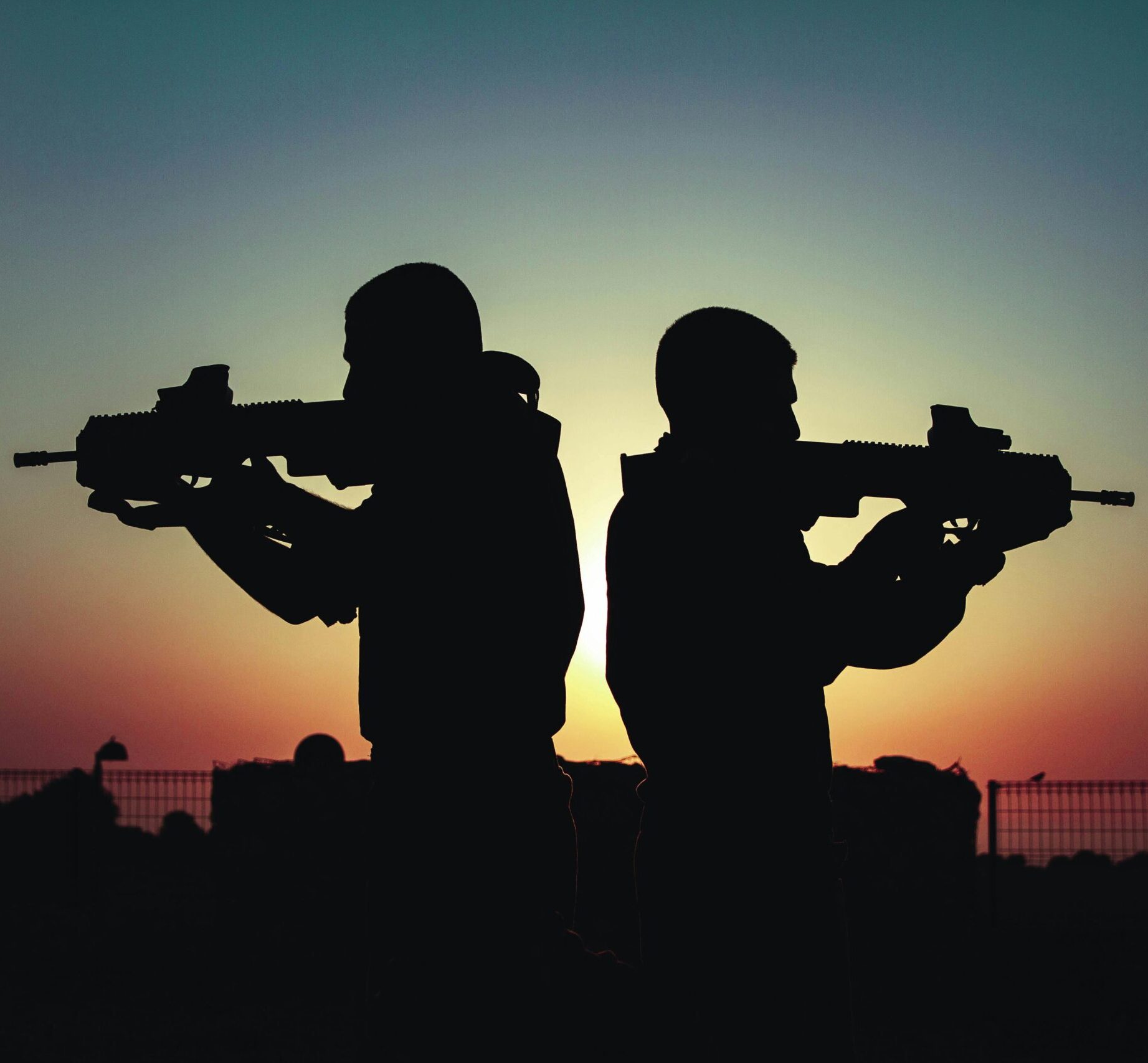 Silhouette of two soldiers with rifles against a vivid sunset sky, creating a dramatic scene.