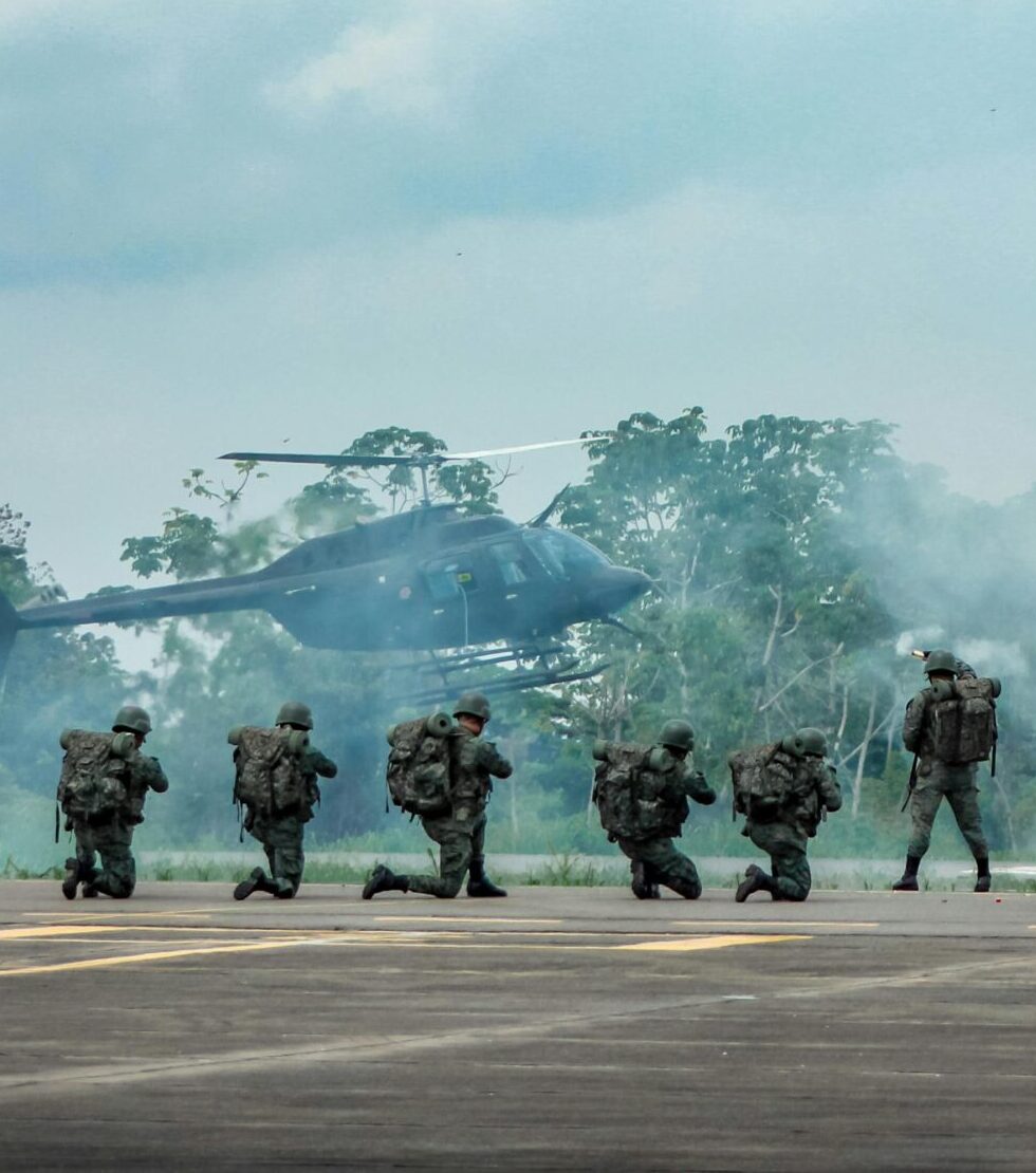 Military personnel in action during a training exercise with helicopter support and weapon artillery outdoors.